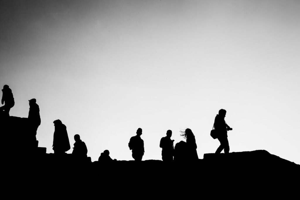 Black and white low angle of unrecognizable silhouettes of travelers walking on staircase of ruins